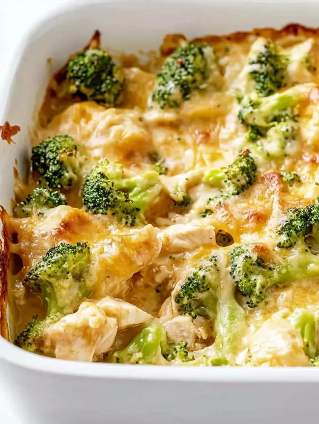 Cheesy broccoli chicken casserole in a white baking dish, featuring tender shredded chicken, fresh green broccoli florets, crispy bacon, and melted cheddar cheese in a creamy sauce